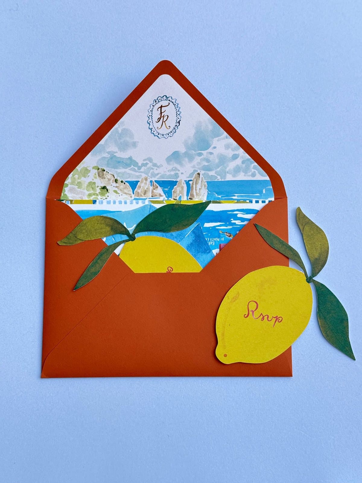 Terracotta envelope with a watercolour liner of the Faraglioni and a monogram, and a lemon-shaped RSVP card